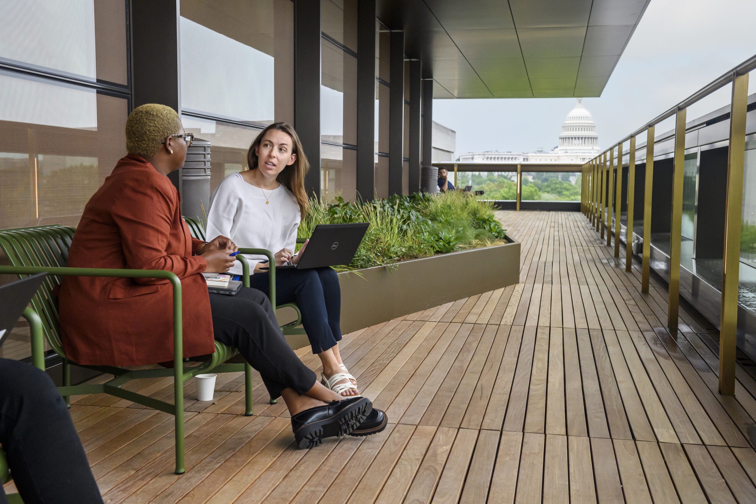Two people sit outside on benches, talking